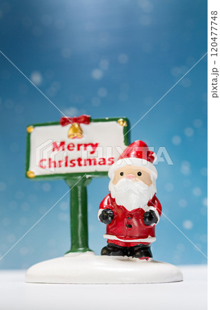 Miniature Santa Claus figurine standing next to a festive Merry Christmas sign Miniature Santa Claus figurine standing next to a festive Merry Christmas sign 120477748