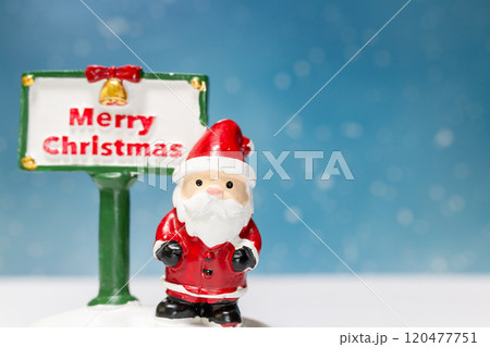Miniature Santa Claus figurine standing next to a festive Merry Christmas sign 120477751
