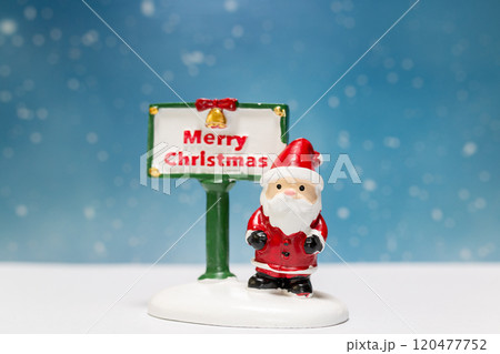 Miniature Santa Claus figurine standing next to a festive Merry Christmas sign 120477752