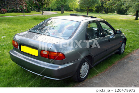Classic dark silver sedan is parked on a grassy patch with trees and foliage in the background, the scene conveys a peaceful, natural setting with vibrant green surroundings 120479972