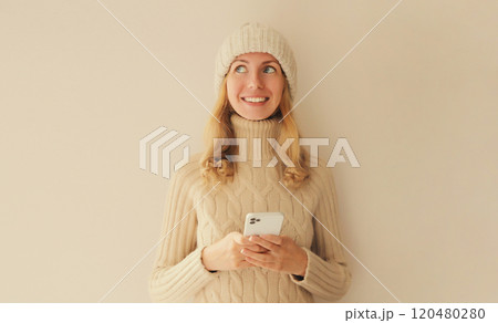Portrait happy smiling young woman with phone in winter hat, white sweater, girl holding smartphone Portrait happy smiling young woman with phone in winter hat, white sweater, girl holding smartphone 120480280
