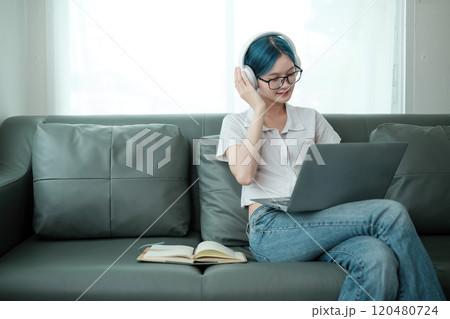 A woman is sitting on a couch with a laptop and headphones on A woman is sitting on a couch with a laptop and headphones on 120480724