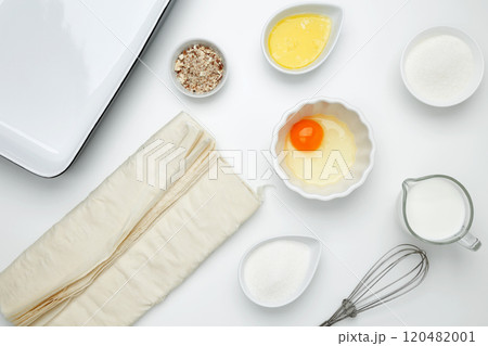 Near baking dish with ingredients, phyllo dough, egg, butter, nuts, and milk on a white background for baking Crinkle Cake 120482001