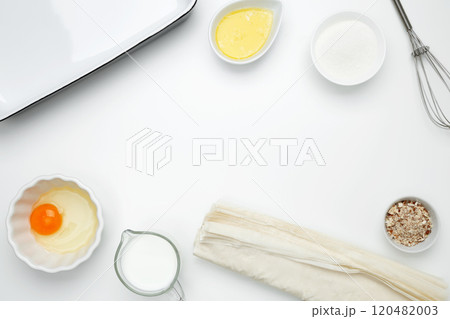 Near baking dish with ingredients, phyllo dough, egg, butter, nuts, and milk on a white background for baking Crinkle Cake Near baking dish with ingredients, phyllo dough, egg, butter, nuts, and milk on a white background for baking Crinkle Cake 120482003