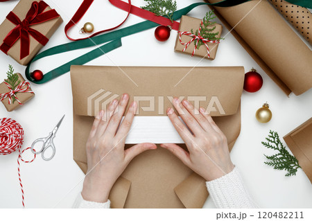 Woman's hands wrapping Christmas gifts with festive decorations in a cozy holiday setting Woman's hands wrapping Christmas gifts with festive decorations in a cozy holiday setting 120482211