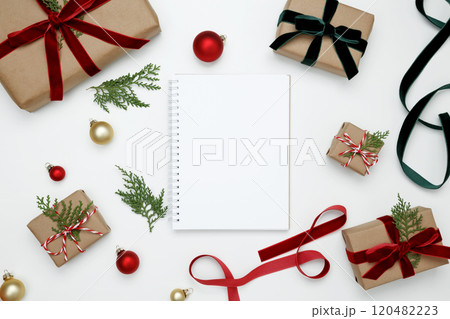 Mockup of white notebook surrounded by wrapped Christmas gifts and thuja branches in a festive setup 120482223