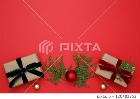 Gifts wrapped in craft paper, Christmas ornaments, thuja branches arranged on red background 120482252