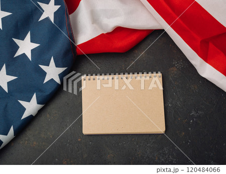 Blank notebook sits on a table next to a red, white, and blue American flag 120484066