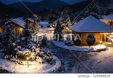 Overhead view of a snowy village nestled in the mountains, with glowing lights and peaceful winter charm. 120484624
