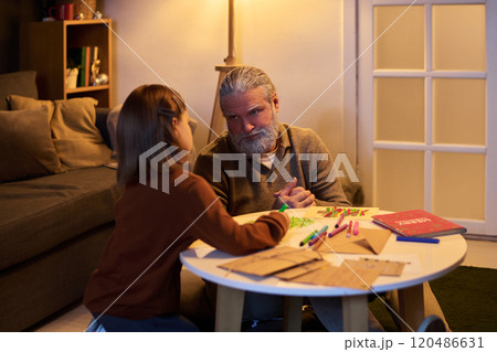 Senior Man Engaging with Small Girl in Cozy Living Room 120486631