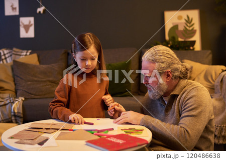 Child and Grandfather Sitting at Table Engaging in Crafting 120486638