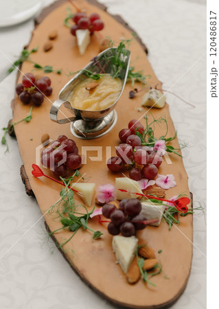 A wooden cutting board with cheese, grapes, and sauce 120486817