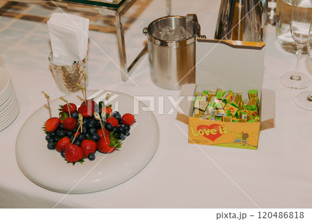 On a table, there is a plate filled with various fruits and a box of candies On a table, there is a plate filled with various fruits and a box of candies 120486818