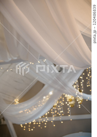 A white curtain hangs from the ceiling of a lit room A white curtain hangs from the ceiling of a lit room 120486839
