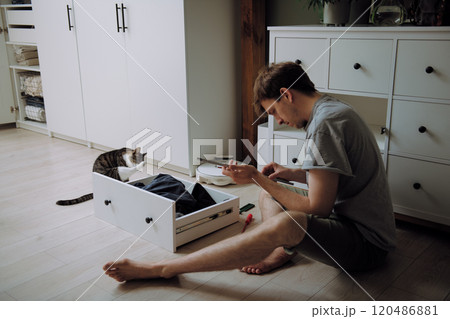 A man sits comfortably on the floor with a cat in a drawer A man sits comfortably on the floor with a cat in a drawer 120486881