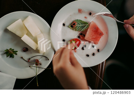 An individual is enjoying a delicious plate of assorted fruit with a fork An individual is enjoying a delicious plate of assorted fruit with a fork 120486903