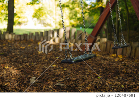 Empty black swing on children playground in the park in autumn season. Missing child. Lonely swing in sunny autumn day. Golden foliage in late fall. Beautiful nature. Empty black swing on children playground in the park in autumn season. Missing child. Lonely swing in sunny autumn day. Golden foliage in late fall. Beautiful nature. 120487691