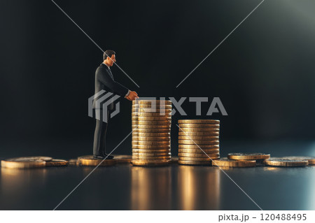 Businessman examining stacks of coins on a reflective surface. Businessman examining stacks of coins on a reflective surface. 120488495