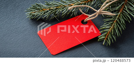 Red tag with pine branches on dark surface, perfect for holiday decoration. 120488573