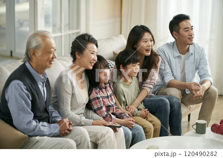 three generation asian family watching tv together at home 120490282