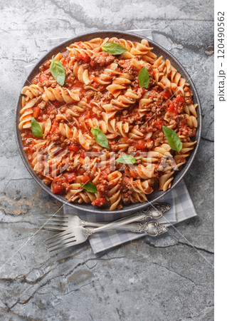 Italian Big Fusilloni bolognese pasta with a beef tomato sauce closeup on the plate. Vertical top view Italian Big Fusilloni bolognese pasta with a beef tomato sauce closeup on the plate. Vertical top view 120490562