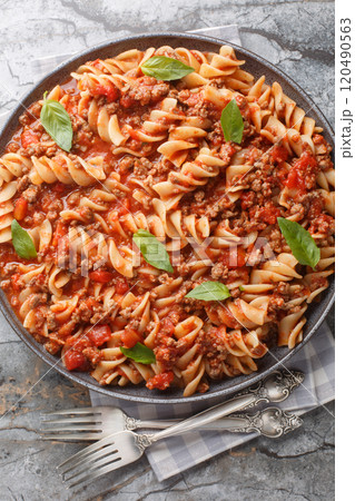Fusilloni bolognese pasta with a hearty meat tomato sauce closeup on the plate. Vertical top view 120490563