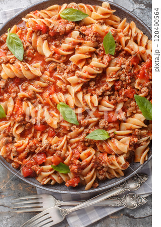Bolognese pasta Fusilli with tomato sauce, ground minced beef, basil leaves closeup on the plate on the table. Vertical top view 120490564