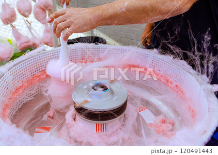 Pink cotton candy being made outdoors using machine pan for preparing delicious treat Pink cotton candy being made outdoors using machine pan for preparing delicious treat 120491443