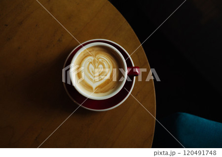 Close up with hot cappuccino with coffee art on the wooden table.A red cup of latte art coffee on natural wood table. Close up with hot cappuccino with coffee art on the wooden table.A red cup of latte art coffee on natural wood table. 120491748