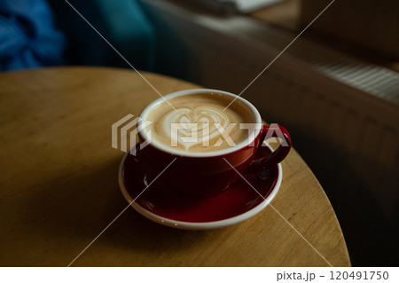 Close up with hot cappuccino with coffee art on the wooden table.A red cup of latte art coffee on natural wood table. 120491750