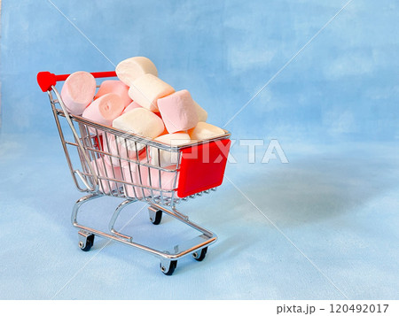 Miniature cart from a supermarket with marshmallows. Blue background 120492017