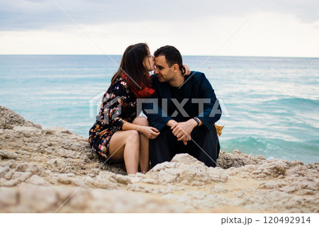 a young couple in love playing with orange stray cat on fabulous rocky coast with turquoise water Ayia Napa, Cyprus 120492914