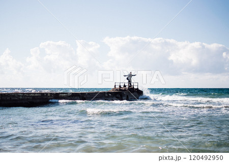 a portrait of a young man on a pier, waves splashing and crashing against the pier 120492950