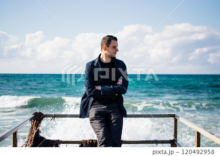 a portrait of a young man on a pier, waves splashing and crashing against the pier 120492958