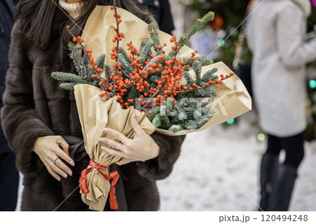 Woman carrying a bouquet of red berries and evergreen branches wrapped in paper. Traditional Christmas decoration Woman carrying a bouquet of red berries and evergreen branches wrapped in paper. Traditional Christmas decoration 120494248
