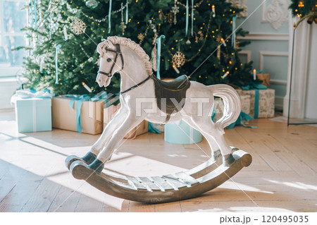 White wooden rocking horse in cozy festive living room on Christmas tree background White wooden rocking horse in cozy festive living room on Christmas tree background 120495035