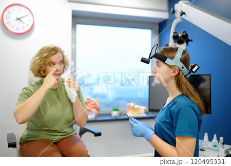 A young woman at an appointment with an otolaryngologist talks about her symptoms. A professional ENT doctor examines a patient. 120495331