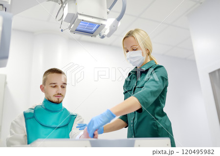 Young man having x-ray shot of broken hand in x ray room in modern clinic. Patient wearing in protect lead apron 120495982