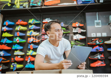A young man is working diligently at a sports shoe store while using a tablet 120499394