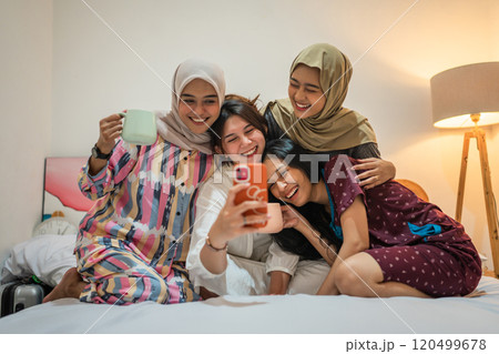 Friends joyfully taking a selfie in a cozy bedroom, sharing precious memories 120499678