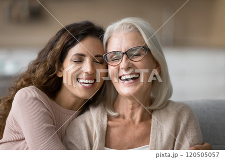 Elderly mother and millennial daughter cuddling seated together on couch Elderly mother and millennial daughter cuddling seated together on couch 120505057