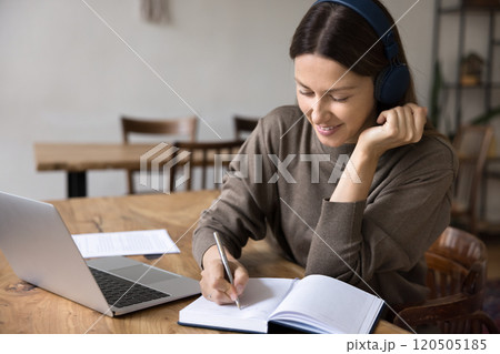 Young woman sits at desk, wearing headphones, writing in notebook Young woman sits at desk, wearing headphones, writing in notebook 120505185