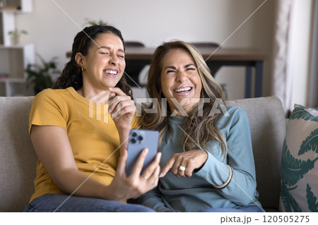 Cheerful laughing senior Hispanic mother and adult daughter using phone 120505275