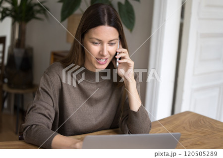 Woman speaking on phone while looking at laptop 120505289