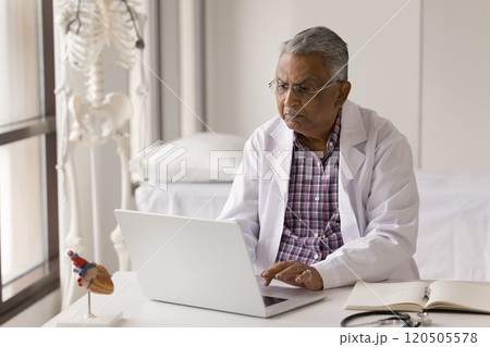 Older Indian cardiologist working on laptop in office 120505578