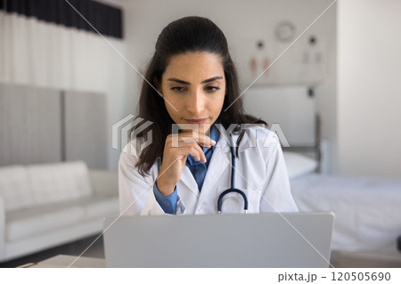 Close up of thoughtful Brazilian doctor using laptop at workplace 120505690