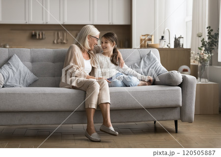 Little girl sits on sofa with granny, laughing, enjoy conversation Little girl sits on sofa with granny, laughing, enjoy conversation 120505887