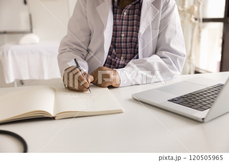 GP doctor sit at desk and writing in medical journal 120505965