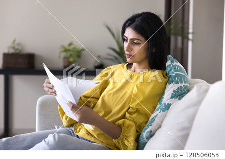 Serious young Indian woman reading legal documents on home couch Serious young Indian woman reading legal documents on home couch 120506053