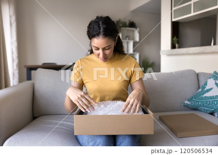 Young Hispanic consumer unwrapping purchase delivered from Internet store 120506534
